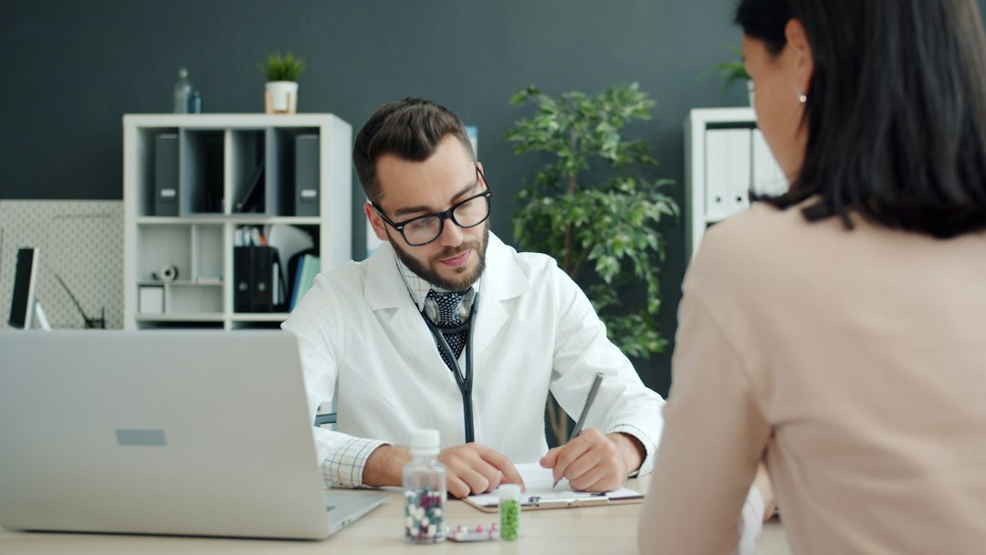 A homeopathic practitioner listening carefully and taking detailed handwritten notes during a patient consultation