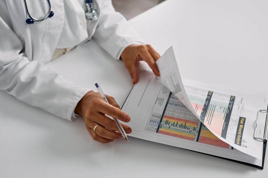 A doctor at a desk making detailed notes in a patient file during a focused clinical review session, methodical and attentive