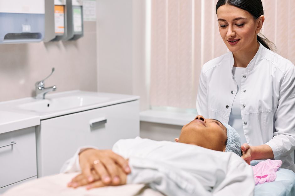 Woman in her forties with naturally radiant healthy skin in a bright clinical consultation room, confident and glowing