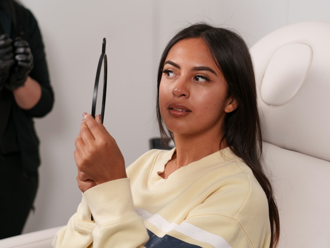 Woman examining her even skin tone in a well-lit mirror, professional and reassuring clinical setting