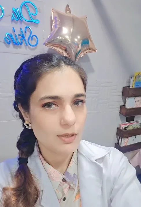female doctor in a professional clinic consultation room, warm approachable expression, wearing a white coat, looking at camera, bright and clean clinical environment
